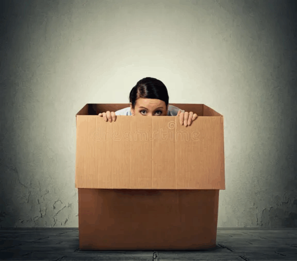 woman hiding in a cardboard box with only her head appearing over the edge of the box.